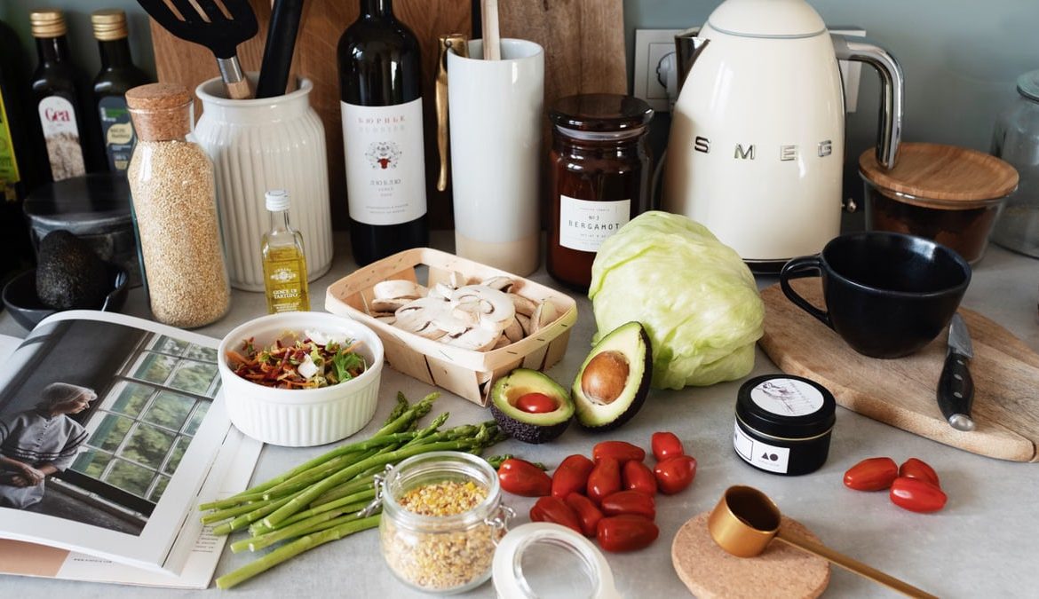 Assorted healthy food and vegetables set locating on gray countertop next to various utensils and appliances during cooking in stylish kitchen